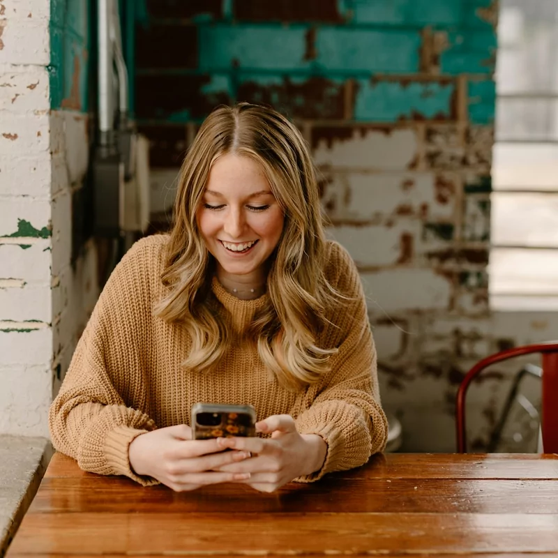 A woman at a caf&eacute; table smiling at her phone